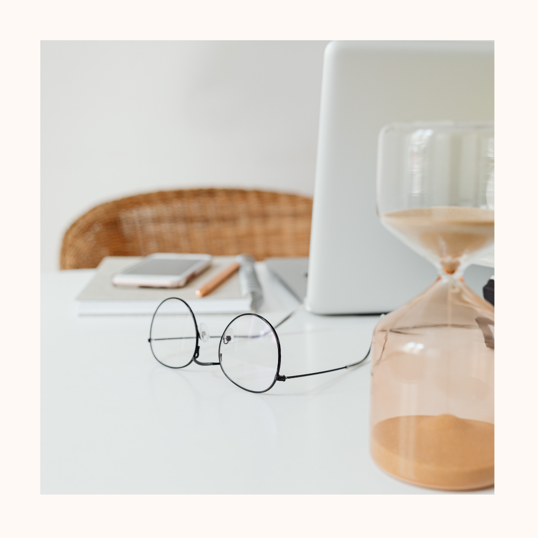 photo avec un ordinateur posé sur un bureau, des lunettes et un sablier